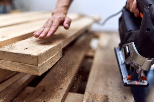Hands of a young woman cutting wooden pallets with a jigsaw