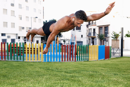 A young man doing calistenia jumps in a colored park