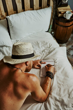 a young man in a hat lying in bed writing in a notebook