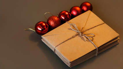 Christmas composition. Craft envelopes and Christmas red balls with copy space. Stack of letters tied with twine on brown background