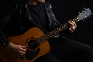 musician with a guitar on a black background in a leather jacket