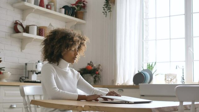 Concentrated African American young freelancer lady with kinky hair sits by table and opens modern laptop closeup slow motion