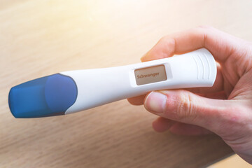Woman checking pregnancy test. Result positive, “Schwanger”