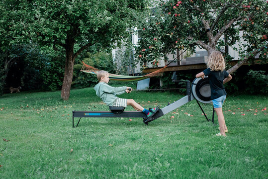 brother and sister using home gym rowing machine in their garden