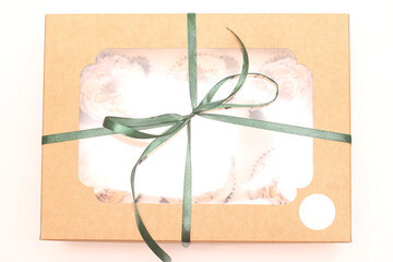 Craft gift box with a transparent top and sweets inside tied with a green ribbon on a white background. Gift studio photo top view