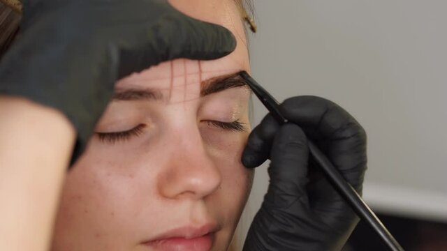 Eyebrow coloring. Professional styling, correction and lamination procedures of female eyebrows in beauty salon. Closeup view 4k video of client face and stylist's hands working in black gloves.
