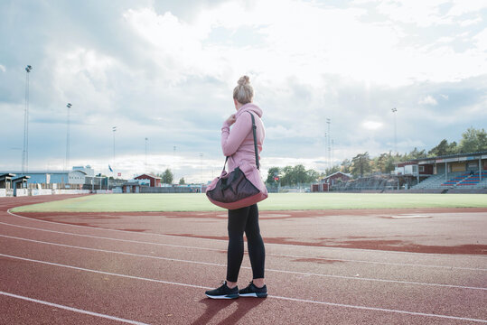 woman stood on a running track with a sports bag waiting