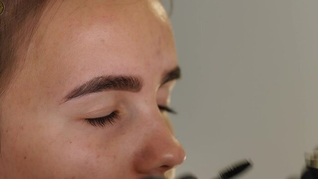 Professional styling, correction and lamination procedures of girl eyebrows in beauty salon. Closeup view of client face and stylist's hands working in gloves. Master removes hair using tweezers.
