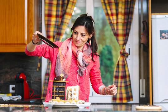 Smiling woman pouring cookie shavings over chocolate cake at kitchen