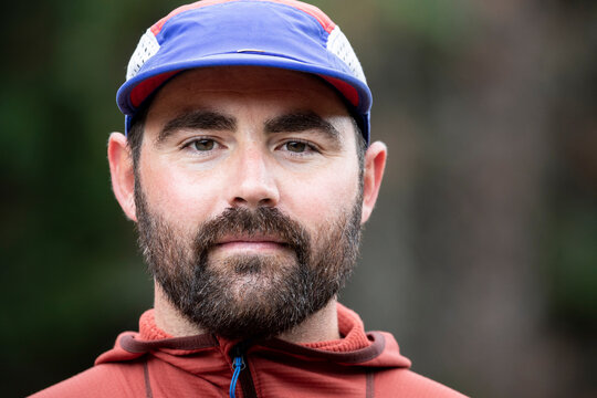 Calm bearded hiker in cap standing in nature and looking at camera