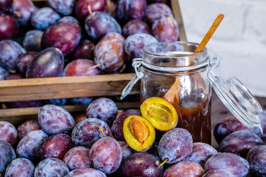 Wooden crate with plums and plum jam in a jar on a wooden table.