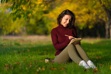 A person write notes sitting on a lawn in an autumn park. Joyful state of mind. Looking for...