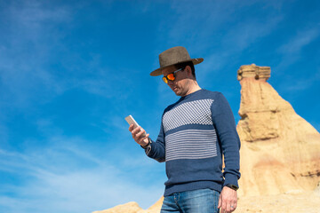 Low angle view of a man with hat and sunglasses standing behind plants while using a mobile phone