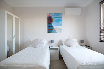 Fototapeta na wymiar Clean twin bedroom in a house with white bed linen and white walls wardrobe with mirrored doors