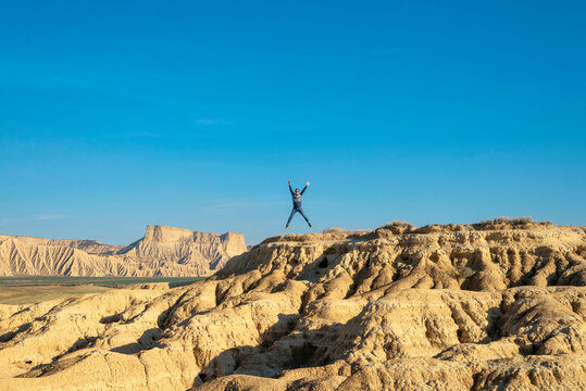 Man with sunglasses jumping with arms raised on a desertic hill against blue sky