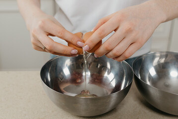A close photo of the hands of a girl who is breaking the organic farm egg above the stainless steel soup bowl in the kitchen.