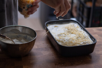 Preparing lasagne, hand pouring grated cheese 