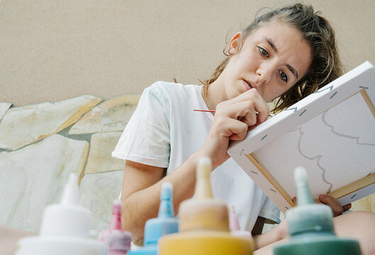 white girl painting with a brush her picture in front of bottle paintings. Horizontal photo