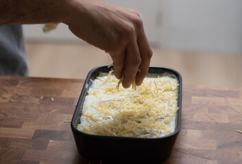 Preparing lasagne, hand pouring grated cheese 