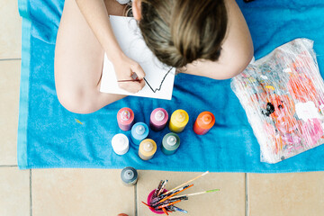 white girl painting with a brush her picture siting on a terrace in front of bottle paintings. Overhead horizontal photo