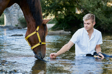 Portrait of a blond young man with a horse on a river