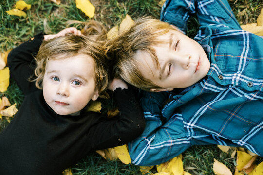 Happy siblings lying on the ground with yellow leaves around them