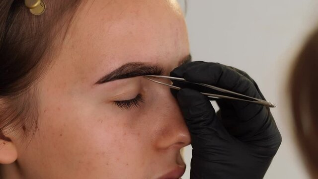 Closeup view 4k video of face of young girl and hands of professional cosmetologist doing depilation and tinting of brows.
