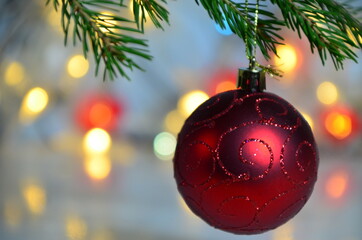 Red Christmas decor ball on green tree branch of a Christmas tree on a background of Christmas lights new year background, no focus, blur, blurry