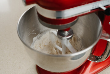 A close photo of a red stand mixer which is whipping butter, almond flour, and wheat flour to the shortcrust pastry in a stainless steel mixing bowl in a kitchen.