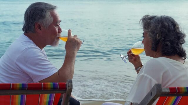 An elderly Asian couple happily sat drinking wine on the beach bed by the sea