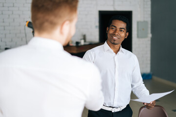 Obraz premium Back view of Caucasian businessman and African American business man signing contract and shaking hands at modern office conference room.