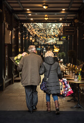Adult couple in love. A couple walking through a shopping area, the man carries a bouquet of flowers and the woman some bags with gifts