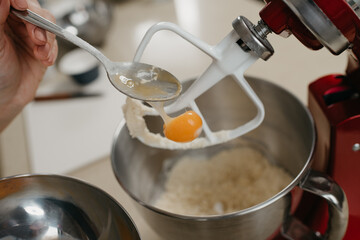 A close photo of the yolk is falling from the spoon into the stainless steel bowl of the red stand mixer with shortcrust pastry.