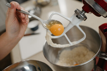A close photo of the yolk is sliding from the spoon into the stainless steel bowl of the red stand mixer with shortcrust pastry.
