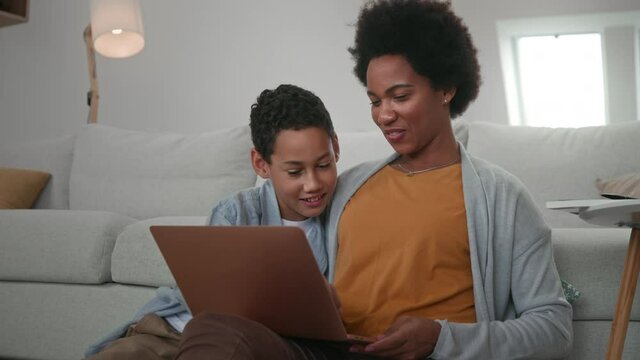 Afro mother and son sitting on floor and using digital tablet