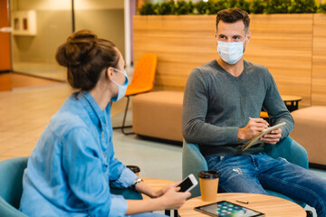 Two young colleagues wearing medical masks against Covid19 talking during coffee break in office