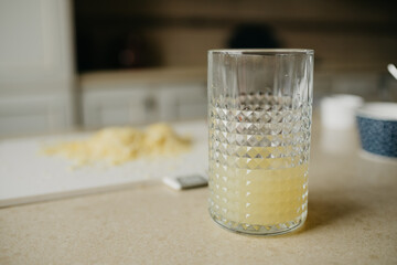 A glass of fresh lemon juice is standing on the table with zest on the background.