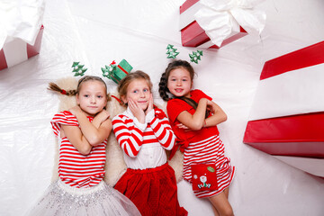 funny little girls friends in Christmas costumes against the background of big red presents.