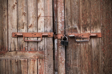 Padlock and rusty metal handles on the gate made of old, textured wood with peeling paint.The texture of a wooden Board. Old board.