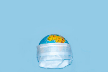 Worldwide pandemic. COVID-19 virus concept with globe in surgical face mask on blue background with place for text and copy space.