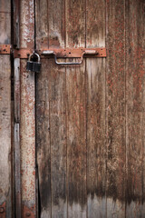 Padlock and rusty metal handles on the gate made of old, textured wood with peeling paint.The...