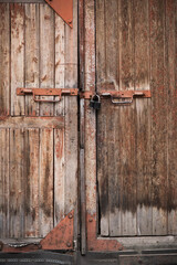 The gate is made of an old, textured Board with peeling paint, rusty metal handles and a barn padlock. Texture of old wood.