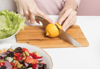 a woman cuts a yellow lemon on a salad cutting Board