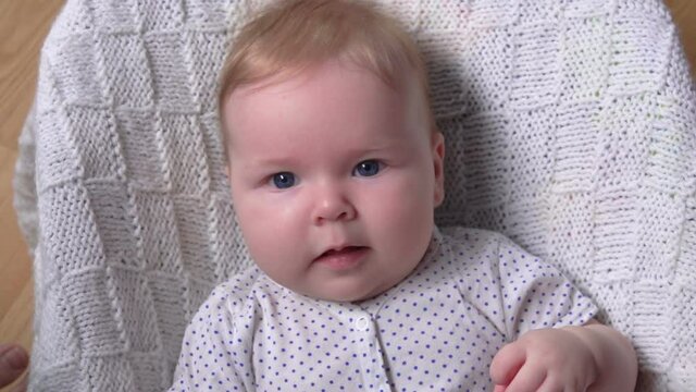 A little adorable blue-eyed baby on a white knitted blanket is looking at the camera