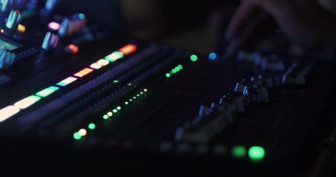 The sound engineer switches the sound modes on the music console, where the volume controls move and the LED lights flash. 