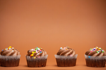 Appetizing chocolate cupcakes with sprinkling on beige background. Sweet dessert. Bakery concept. Elegant food. Sweets for coffee or tea. Space for text.
