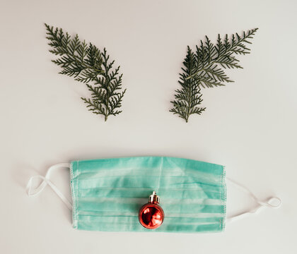 Creative and minimal coronavirus christmas concept. Reindeer face made of Christmas decoration and pine branches with mask on white backgroud. Covid during Christmas season concept. Flat lay top view.