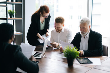 Young mixed race employees listening to confident female team leader. Business team of dedicated multi-ethnic of businesspeople discussing project while working together desk in office.