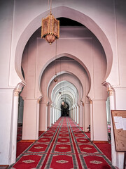 The interior Islamic beauty of the Koutoubia mosque in Marrakesh. The mosque has red Moroccan carpets laid down on the ground with white arches and a long hallway