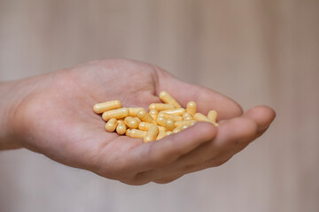 Male hand holds yellow capsules with medicine.